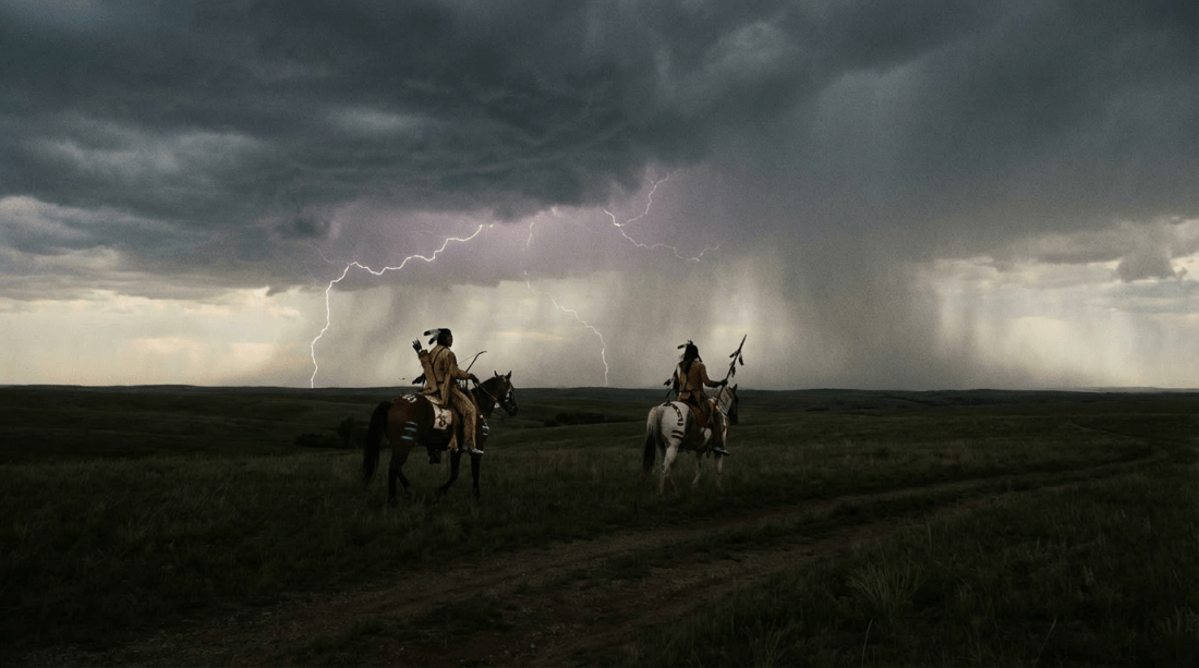 Two cowboys on horseback silhouetted against a dramatic lightning storm on the open plains.